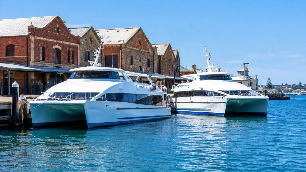 Due catamarani passeggeri bianchi ormeggiati a un molo di Fremantle davanti a vecchi magazzini portuali in mattoni