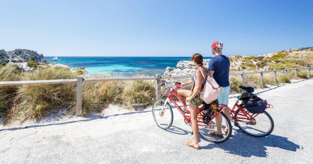Due ciclisti con bici a noleggio rosse a un belvedere su una baia turchese a Rottnest Island